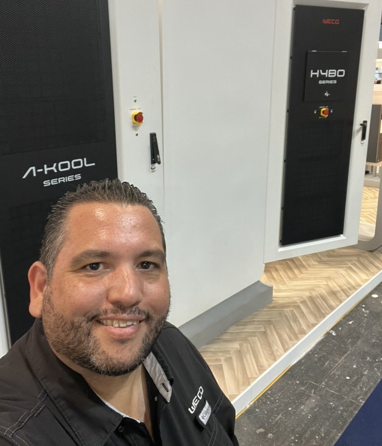 Ricardo Caro Mateo davanti all’armadio di batterie WeCo A-Kool 241 e all’inverter WeCo HYBO TL Series, presso lo stand di WeCo a Genera 2025