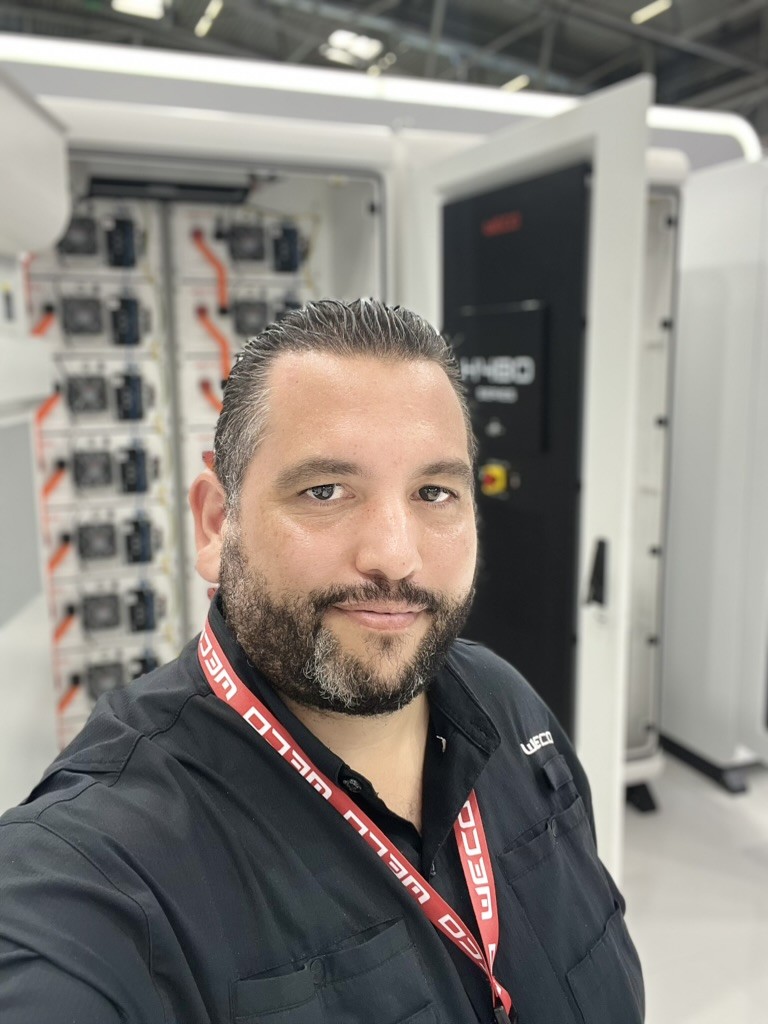 Ricardo Caro Mateo davanti a un armadio di batterie e all’inverter WeCo HYBO TL Series, presso lo stand di WeCo a Intersolar Europe 2026