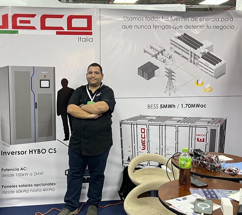 Ricardo Caro Mateo a braccia conserte presso lo stand di WeCo a Oil & Power Ecuador 2024, accanto ai pannelli dell’inverter HYBO CS e del sistema BESS da 5 MWh