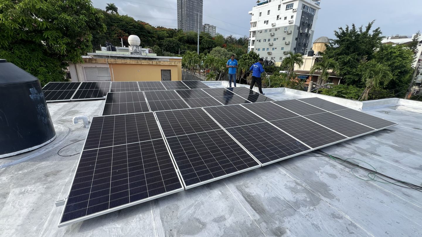 Paneles solares recién instalados en una azotea urbana con dos técnicos al fondo